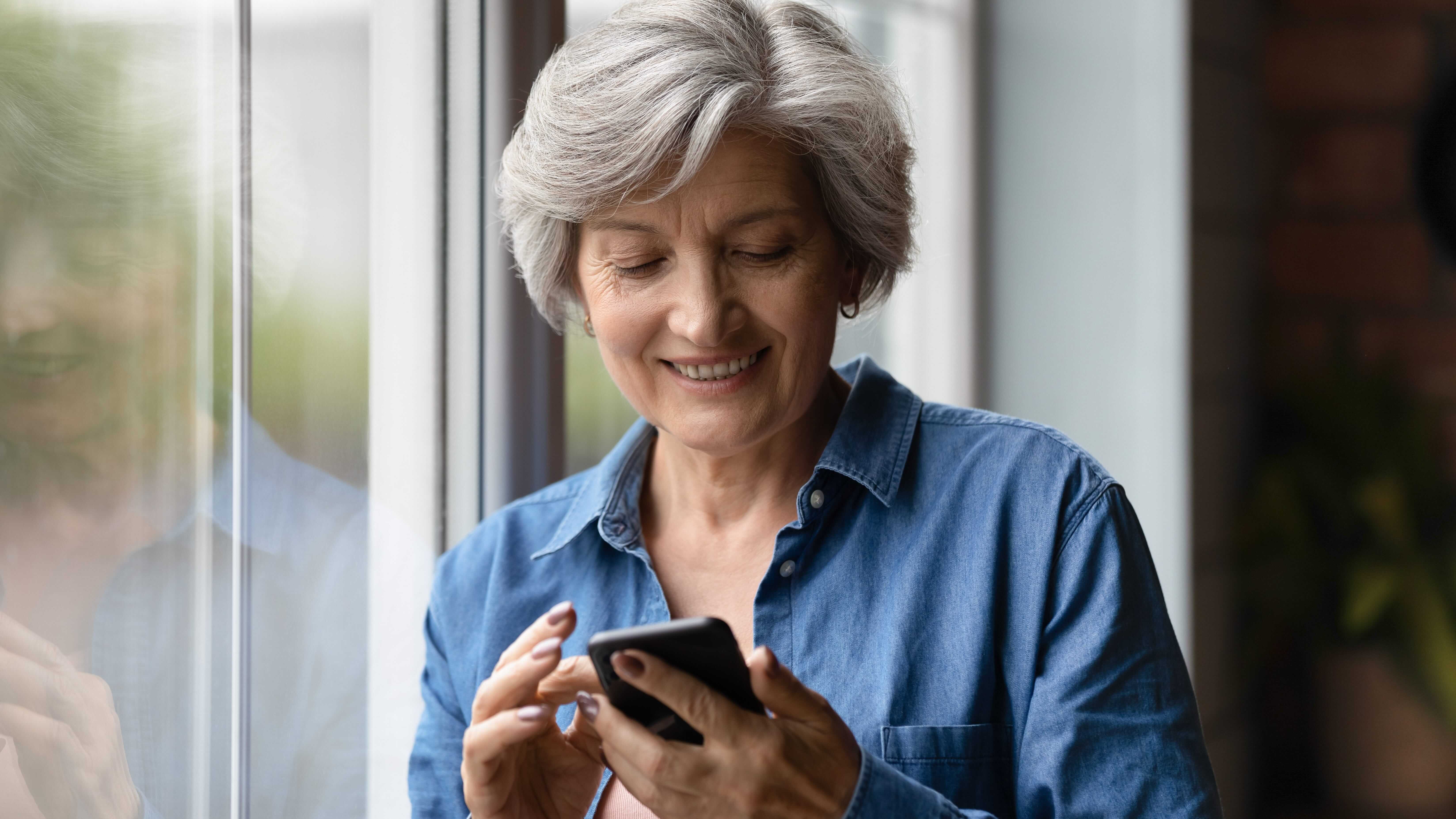 Woman standing by the window smiling at her phone